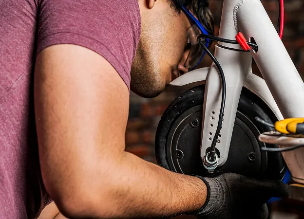Technicien réparant la chaîne et la roue d’une trottinette électrique en atelier